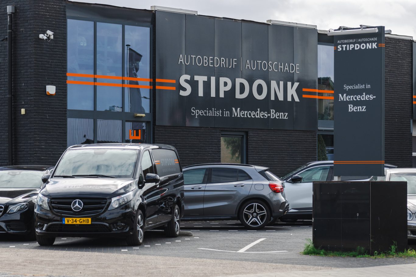 De buitenkant van autobedrijf Stipdonk. Je ziet de gevel met daarop "Autobedrijf en Autoschade Stipdonk. Specialisatie in Mercedes-Benz"
